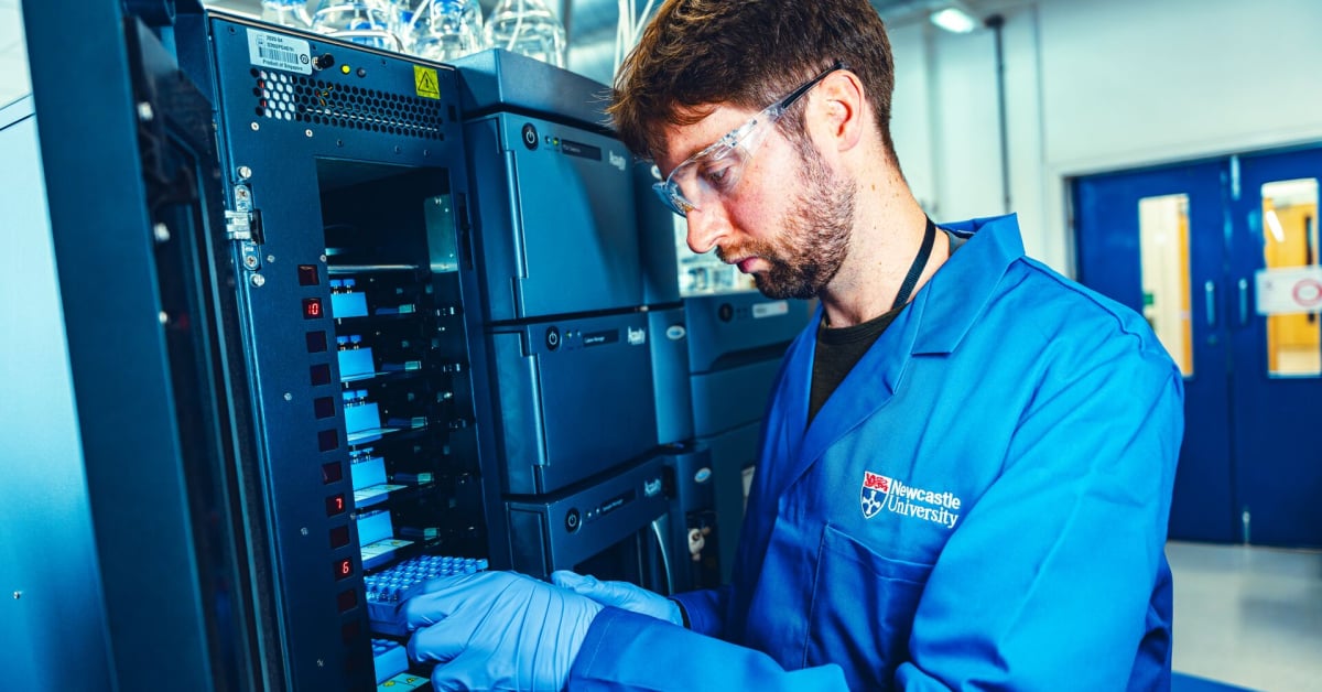 A man in a blue lab coat, blue gloves, and eye protectors uses the analytical facilities at Newcastle University