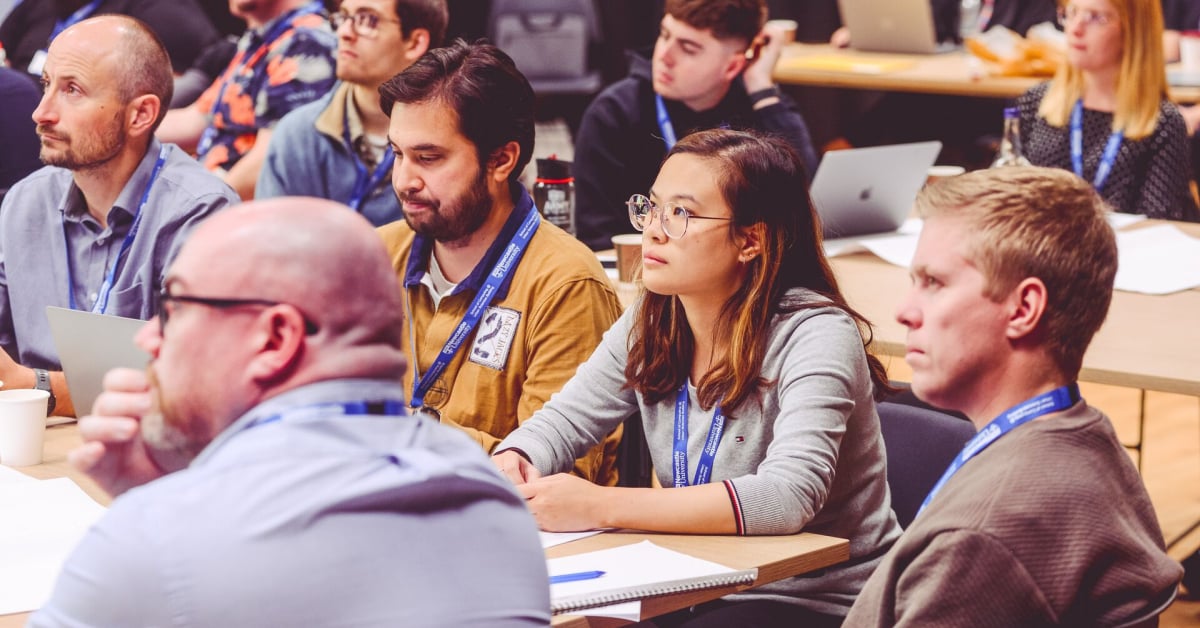 A group of individuals wearing blue lanyards face to the left, as if listening to a talk.