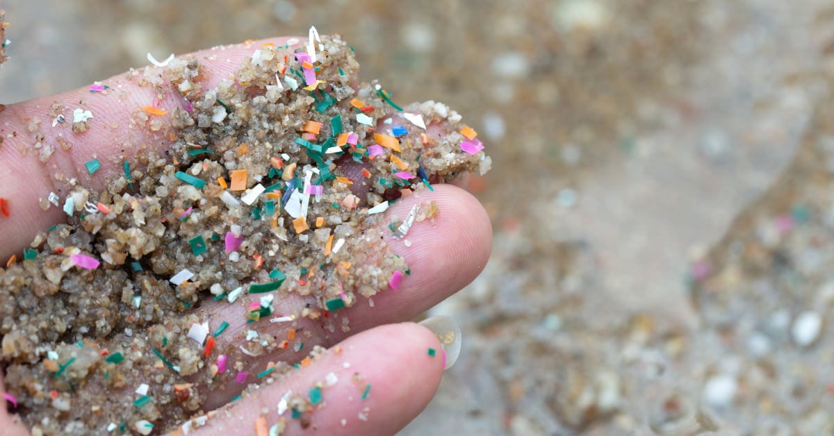 A hand holding sand filled with microplastics.