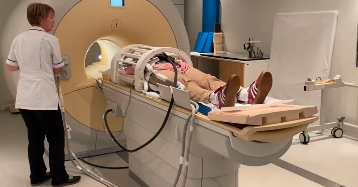 A patient lies in an MRI machine in preparation for a scan, with a doctor standing by.